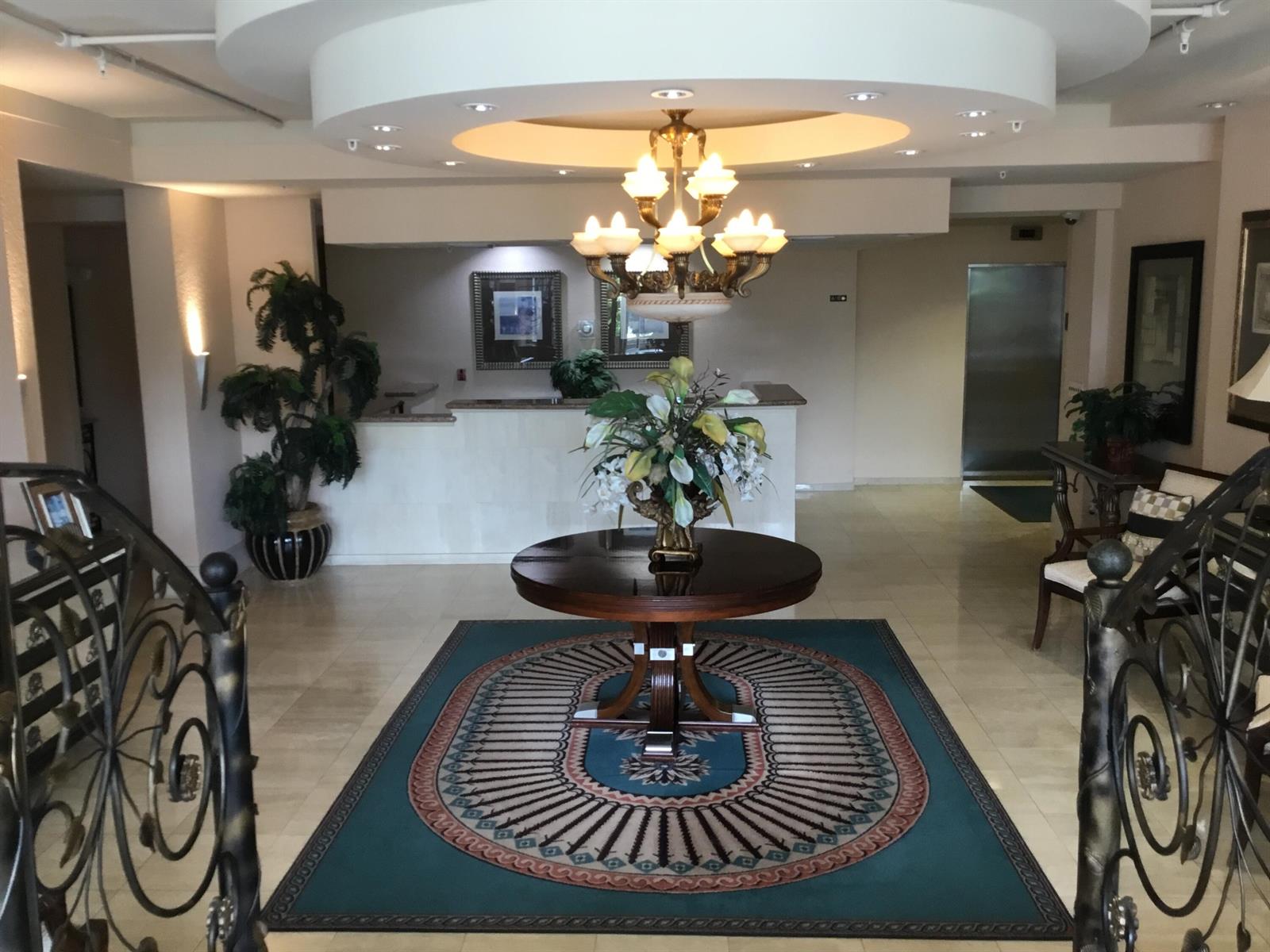 A hotel lobby features a central round table, a decorative chandelier, and a patterned area rug — 1000 Spanish River Road # 3c, Boca Raton FL 33432, BOCA RATON, FL