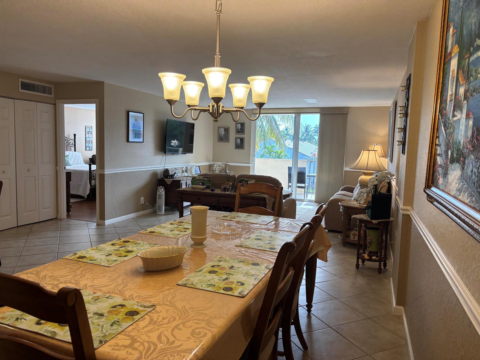 A dining area with a chandelier and table leads into a living room with balcony access — 1000 Spanish River Road # 3c, Boca Raton FL 33432, BOCA RATON, FL