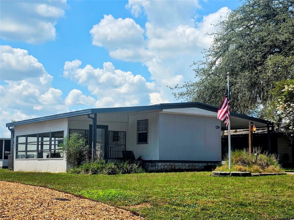 A single-story manufactured home with a white exterior, a front porch, and an American flag — 730 ROYAL PALM AVENUE, LADY LAKE, FL