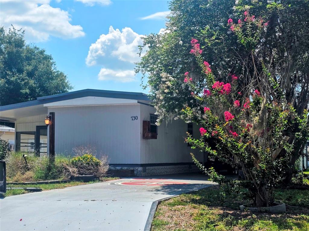 A single-story manufactured home features light siding, a driveway, and a blooming crape myrtle tree — 730 ROYAL PALM AVENUE, LADY LAKE, FL