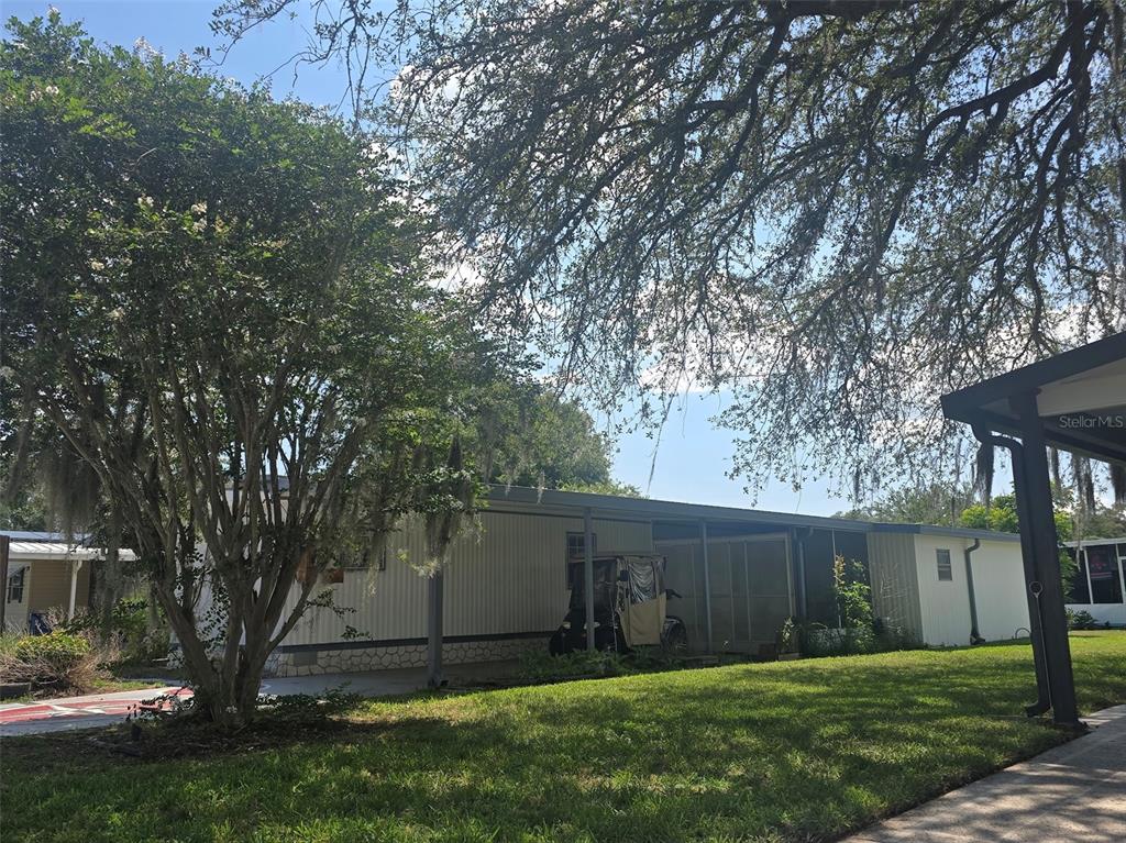 A mobile home with a covered carport and a large tree in the front yard — 730 ROYAL PALM AVENUE, LADY LAKE, FL