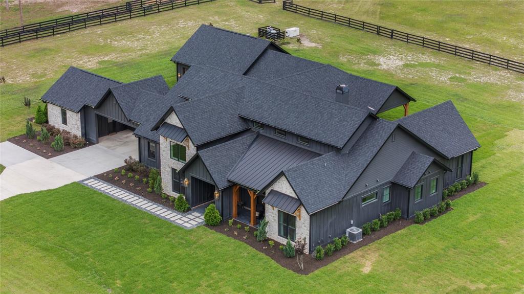 An aerial view of a modern farmhouse with dark siding, stone accents, and a shingled roof — 23741 RIDGE LINK ROAD, EUSTIS, FL