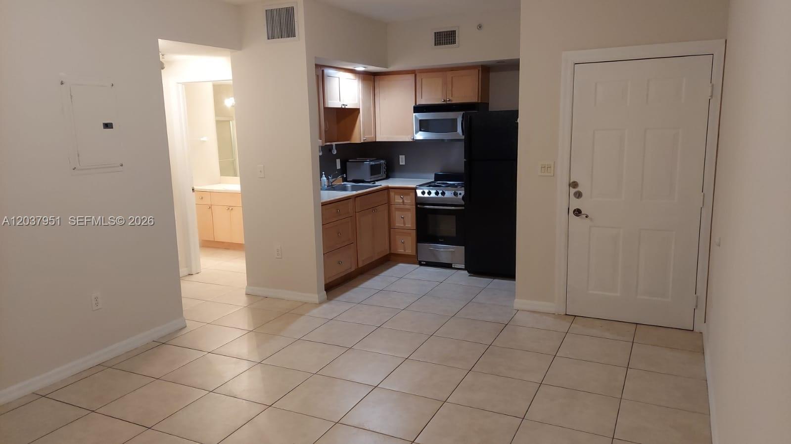 This kitchen features light wood cabinets, black appliances, and tile flooring, with an adjacent laundry area — 2630 SW 28th St # 14, Miami FL 33133, MIAMI, FL