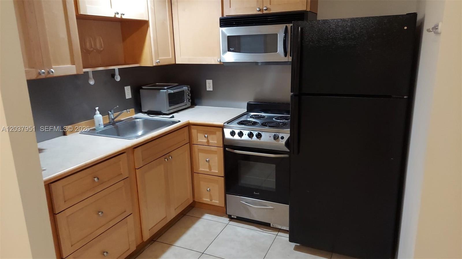 A tiled living area leads to a small kitchen with black appliances and wooden cabinets — 2630 SW 28th St # 14, Miami FL 33133, MIAMI, FL