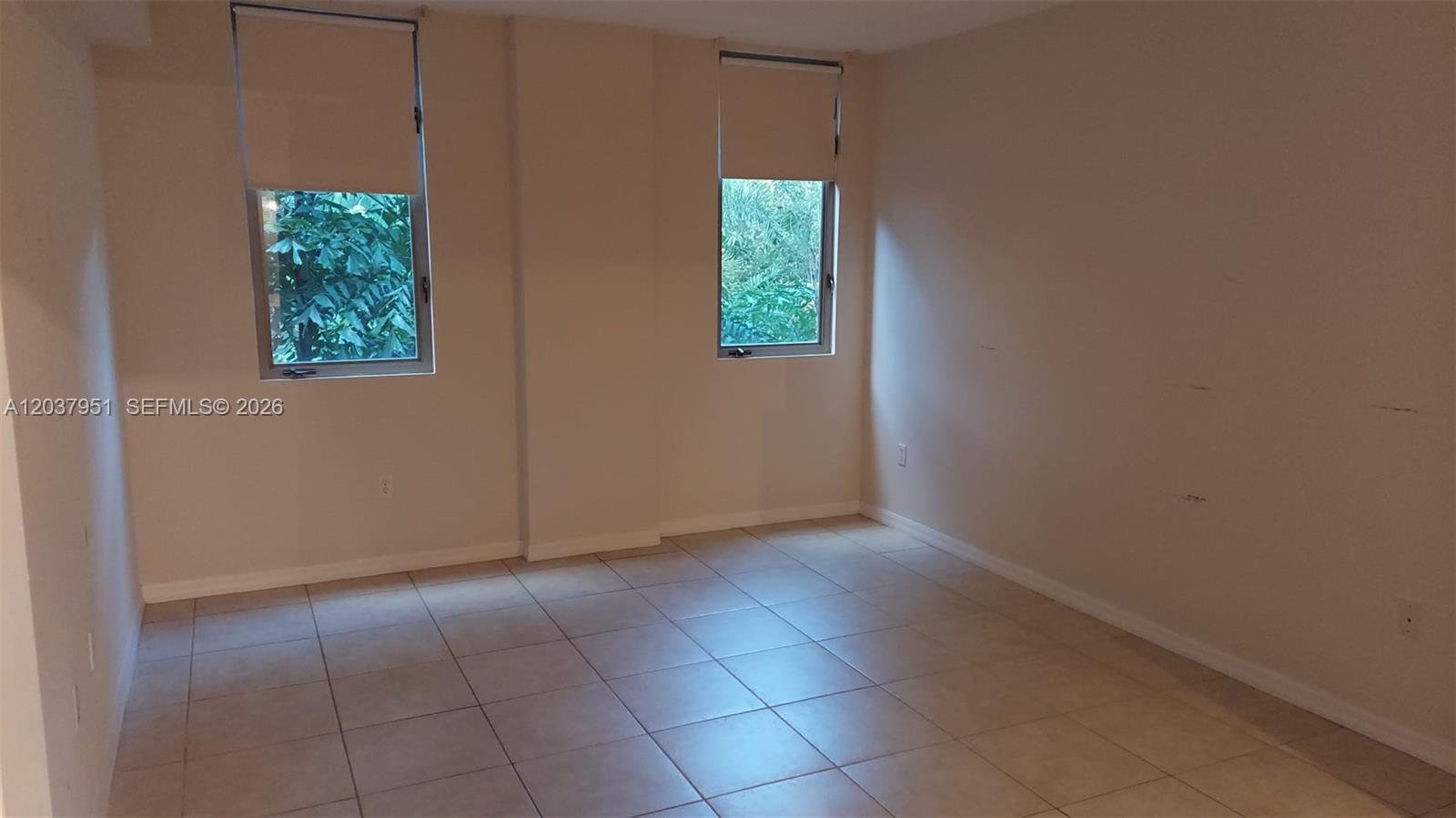 An empty room features white walls, beige tile flooring, and two windows with blinds — 2630 SW 28th St # 14, Miami FL 33133, MIAMI, FL