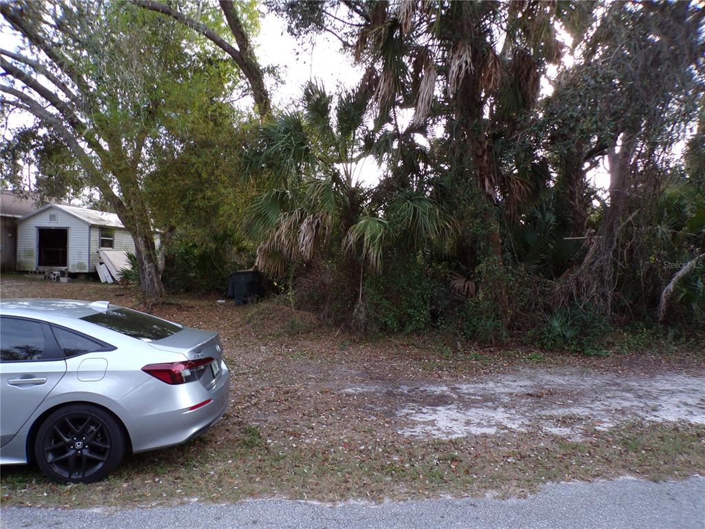 A silver sedan is parked on a dirt lot next to a small shed and trees — TEPEE AVENUE, NORTH PORT, FL
