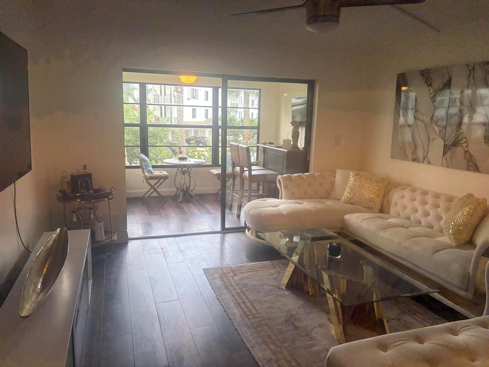 A living room with a tufted sectional, glass coffee table, and sliding doors to a balcony — 9355 SW 8th Street # 225, Boca Raton FL 33428, BOCA RATON, FL