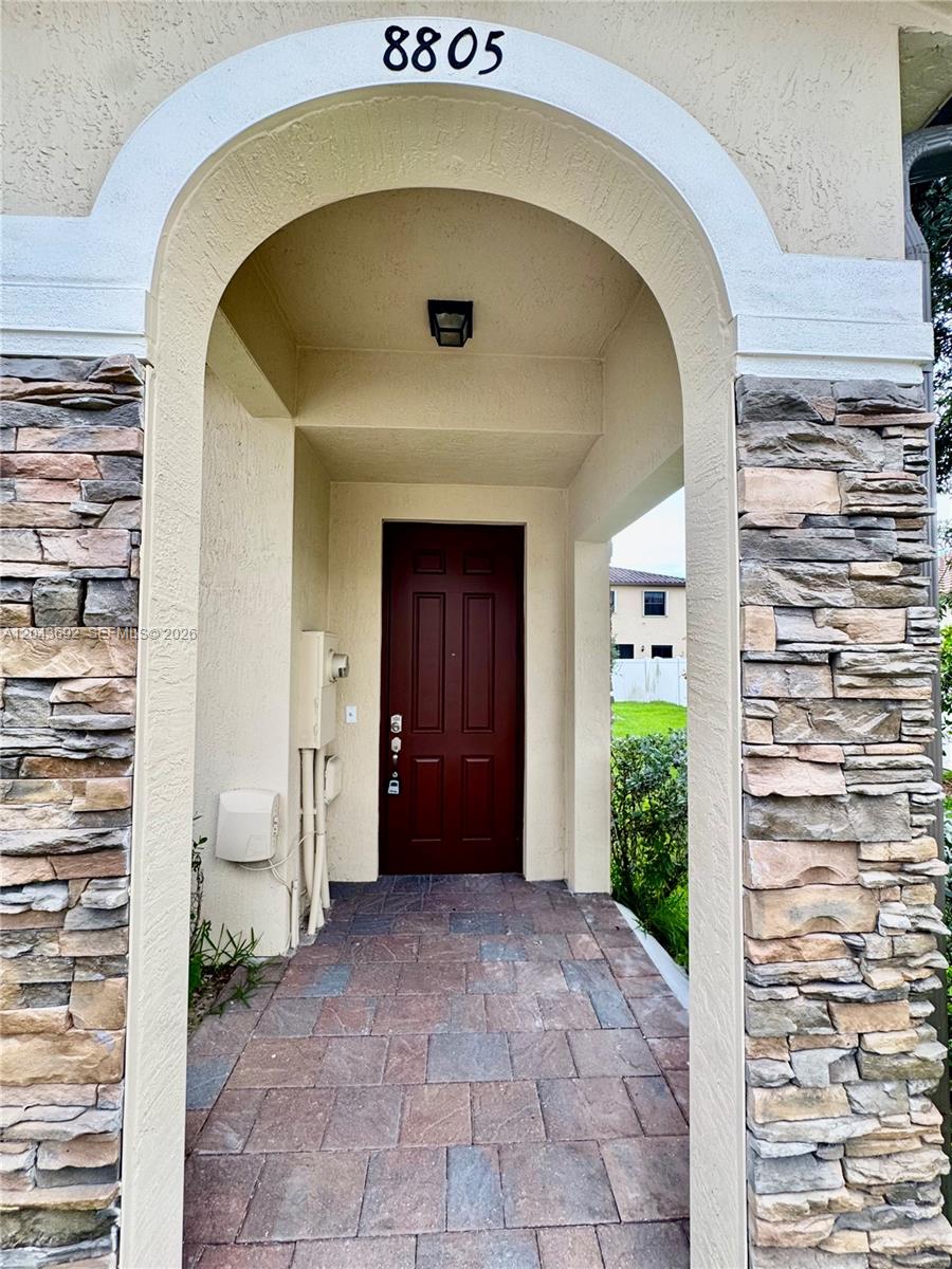 A covered entryway features a dark red door, stone veneer columns, and a paved floor — 8805 W 35th Ave, Hialeah FL 33018, HIALEAH, FL