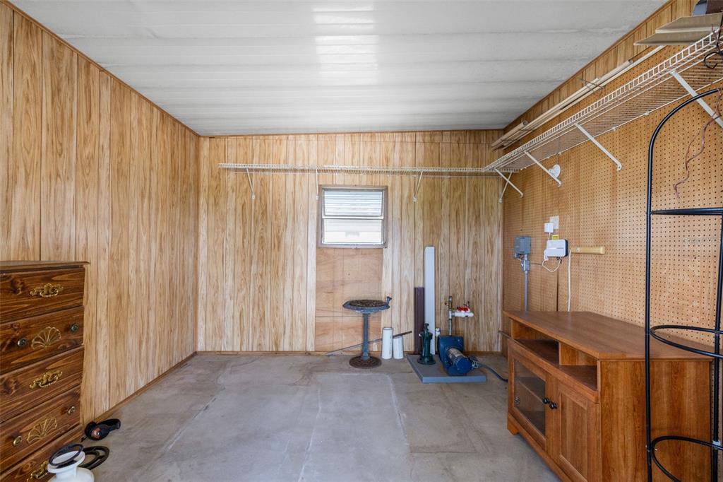 A utility room with wood-paneled walls, a concrete floor, a water pump, and storage shelving — 3217 RAINBOW ROAD, TAVARES, FL