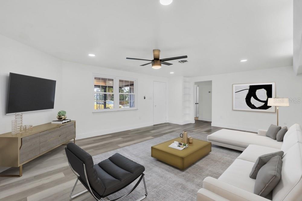 A modern living room features white walls, wood-look flooring, a sectional sofa, and a television — 456 SANDLEWOOD DRIVE, VENICE, FL
