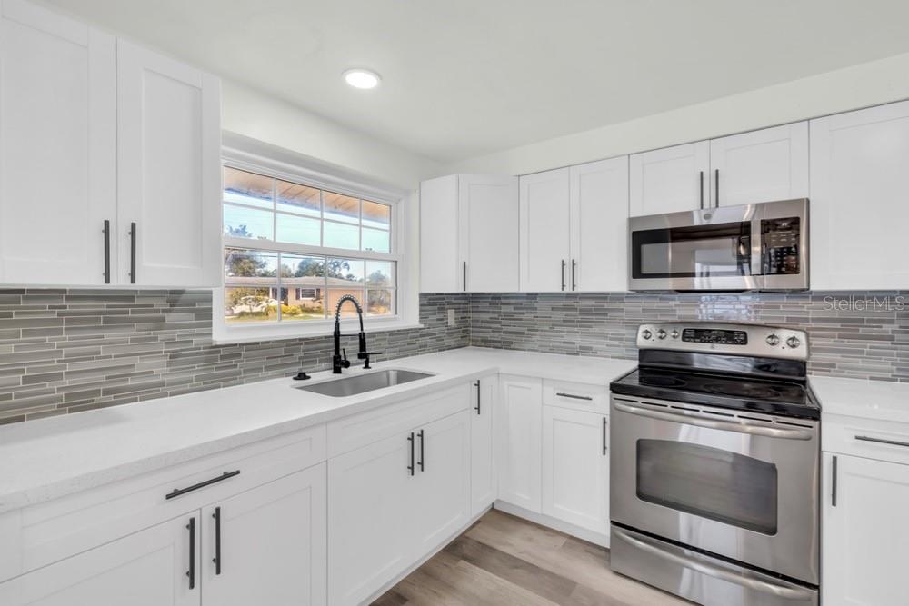A kitchen with white cabinets, stainless steel appliances, a gray tile backsplash, and white countertops — 456 SANDLEWOOD DRIVE, VENICE, FL