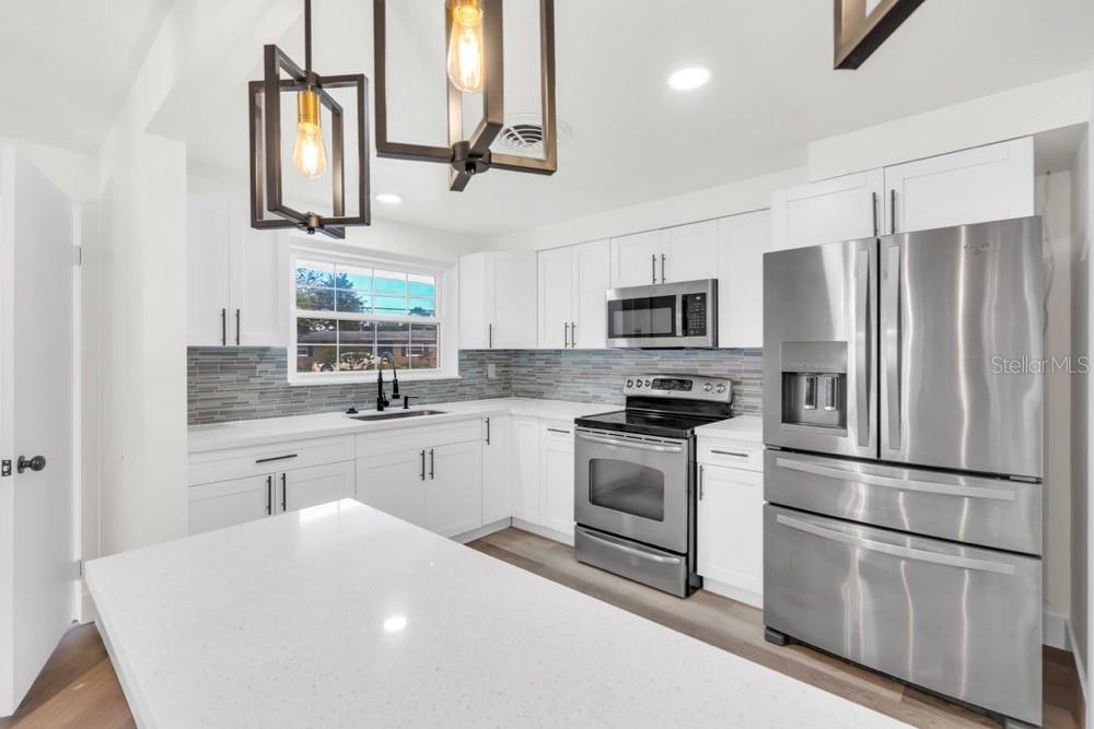 A modern kitchen features white cabinets, stainless steel appliances, a quartz island, and tile backsplash — 456 SANDLEWOOD DRIVE, VENICE, FL