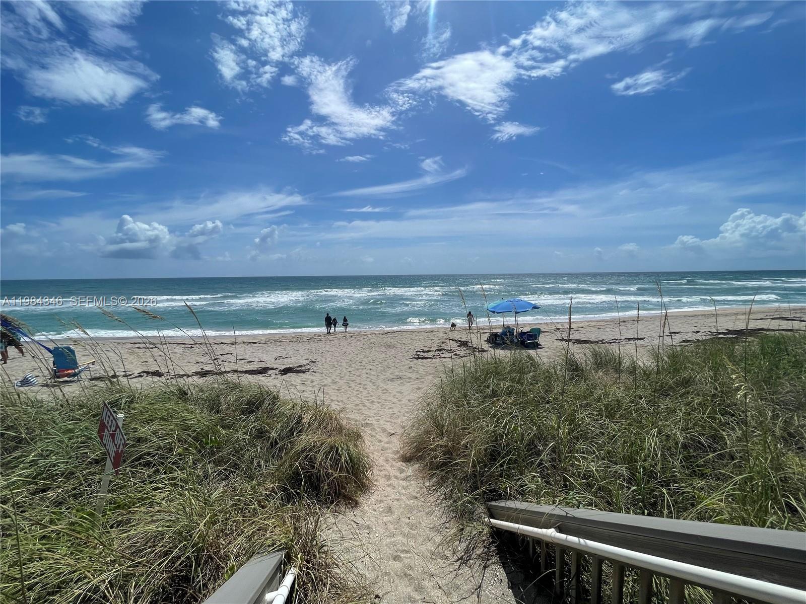 A sandy path leads from wooden stairs through dune grass to a beach with people — 10200 S Ocean Dr # 504, Jensen Beach FL 34957, JENSEN BEACH, FL