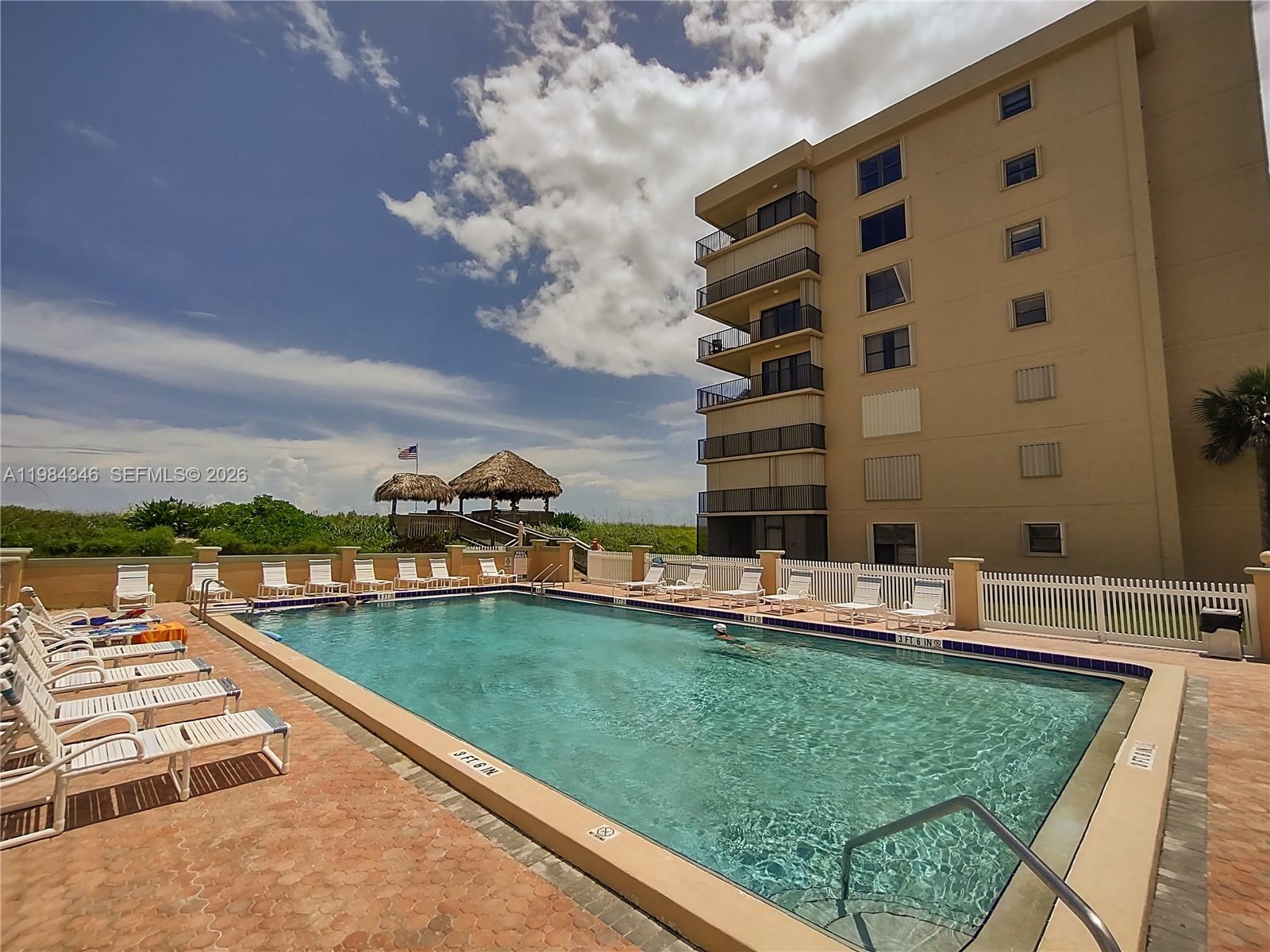 A rectangular swimming pool sits on a patio next to a multi-story tan building — 10200 S Ocean Dr # 504, Jensen Beach FL 34957, JENSEN BEACH, FL
