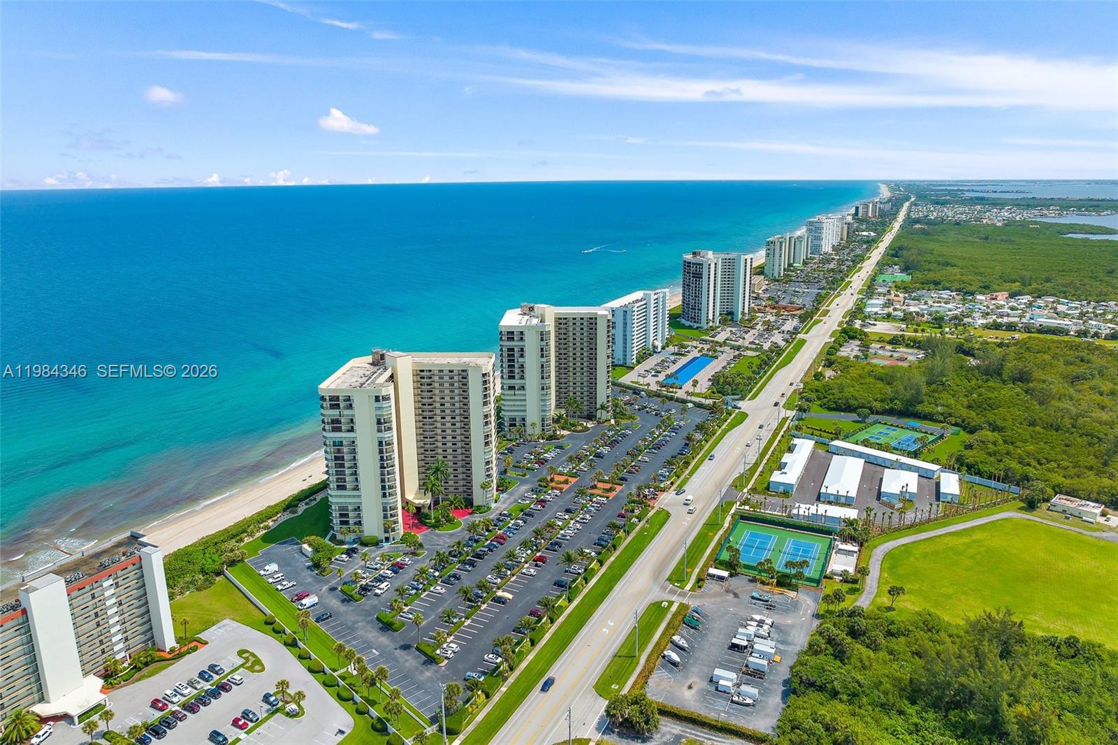 An aerial view shows high-rise residential buildings along a coastline with parking lots and tennis courts — 10200 S Ocean Dr # 504, Jensen Beach FL 34957, JENSEN BEACH, FL