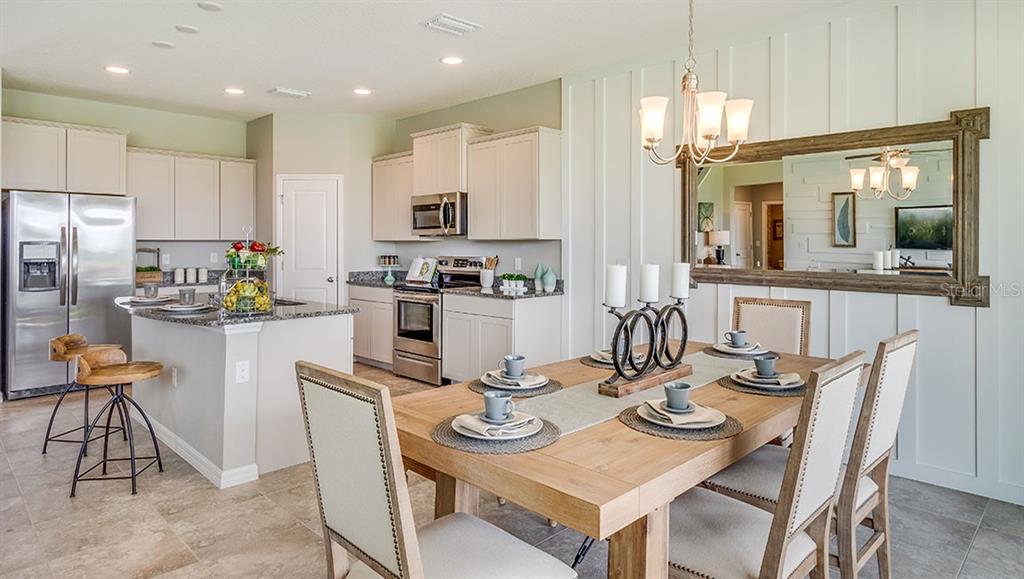 A dining area with a wooden table and chairs sits adjacent to a modern kitchen — 9455 BELLA MAR TRAIL, PARRISH, FL