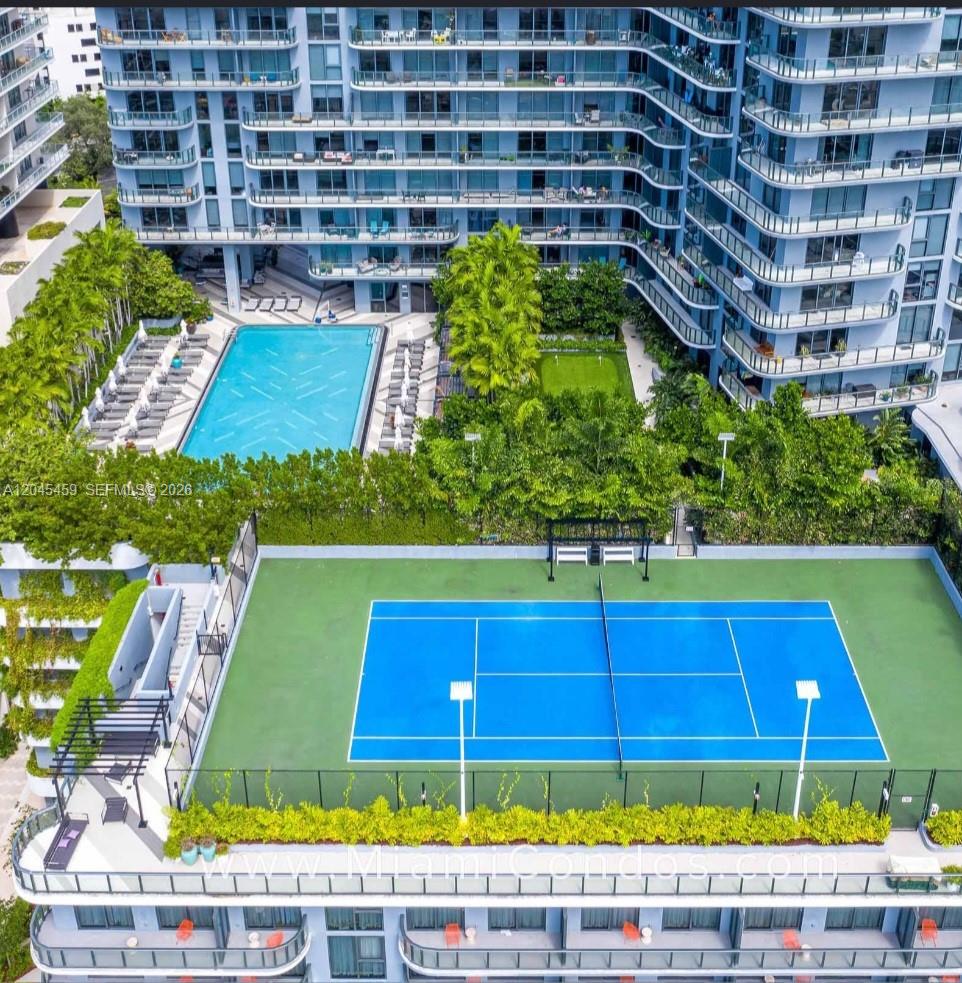 An aerial view shows a tennis court, a swimming pool, and a multi-story residential building — MIAMI, FL