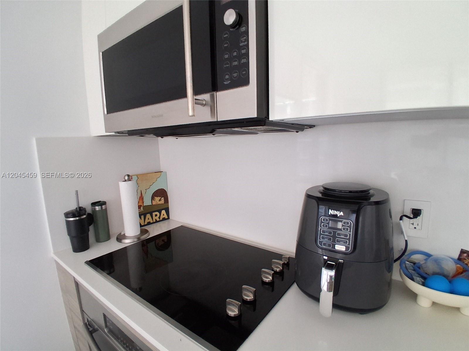 A kitchen counter features a black glass cooktop, a microwave, and a Ninja air fryer — MIAMI, FL