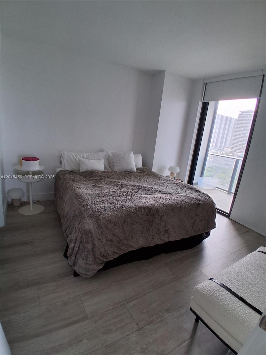 A bedroom features a bed with a brown fuzzy blanket, light wood flooring, and a balcony — MIAMI, FL