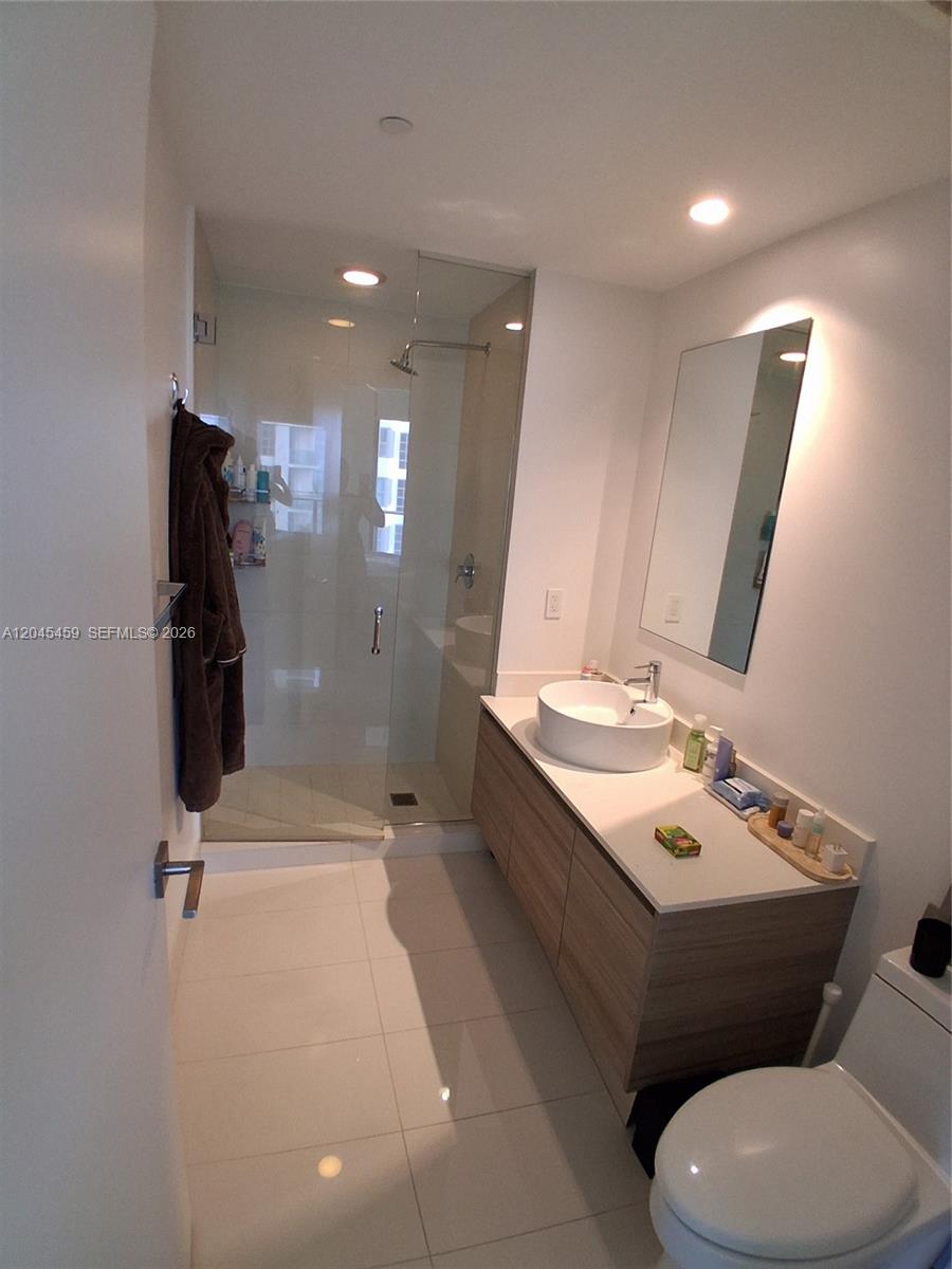 A modern bathroom features a glass-enclosed shower, a floating wood vanity, and white tile flooring — MIAMI, FL