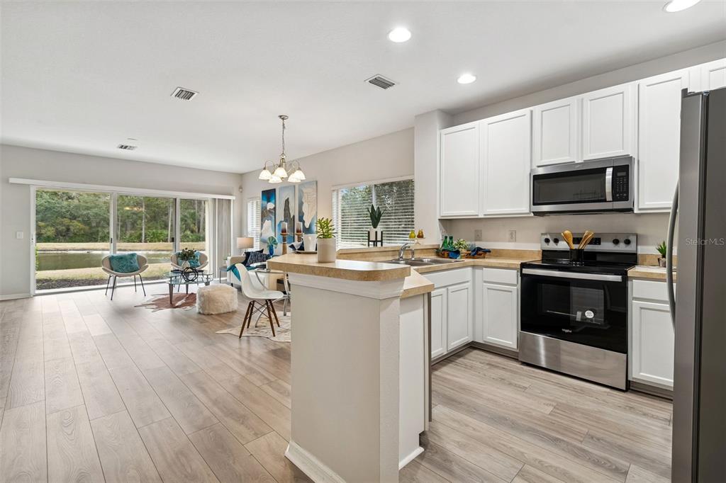 A kitchen with white cabinets and stainless steel appliances overlooks a living area with water views — 20461 BERRYWOOD LANE, TAMPA, FL