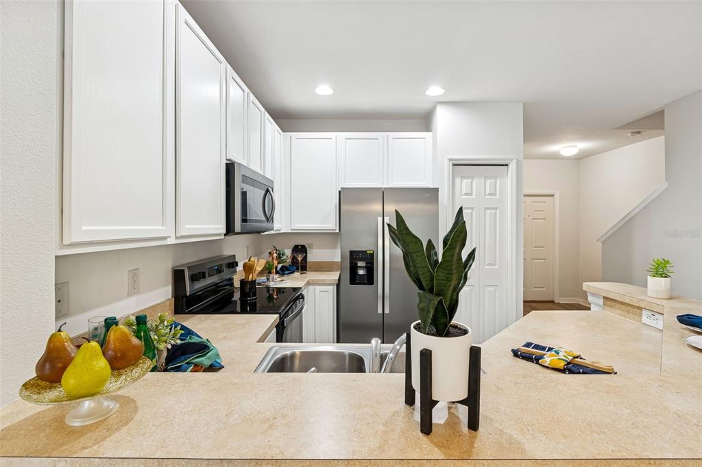 A kitchen features white cabinets, stainless steel appliances, and a beige countertop breakfast bar — 20461 BERRYWOOD LANE, TAMPA, FL