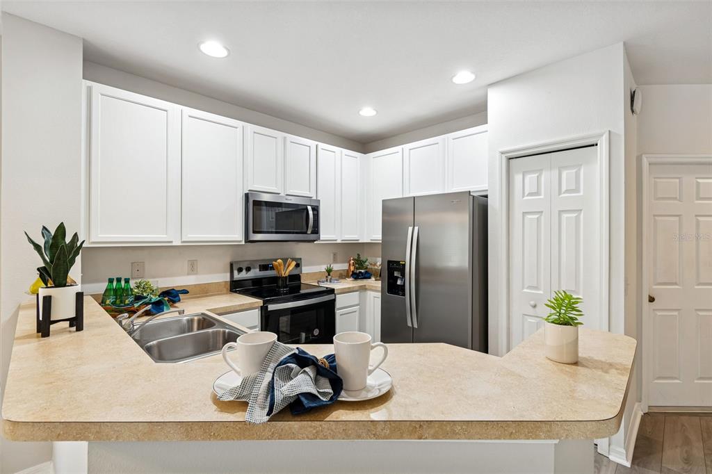 A kitchen features white cabinets, stainless steel appliances, and a tan laminate breakfast bar — 20461 BERRYWOOD LANE, TAMPA, FL
