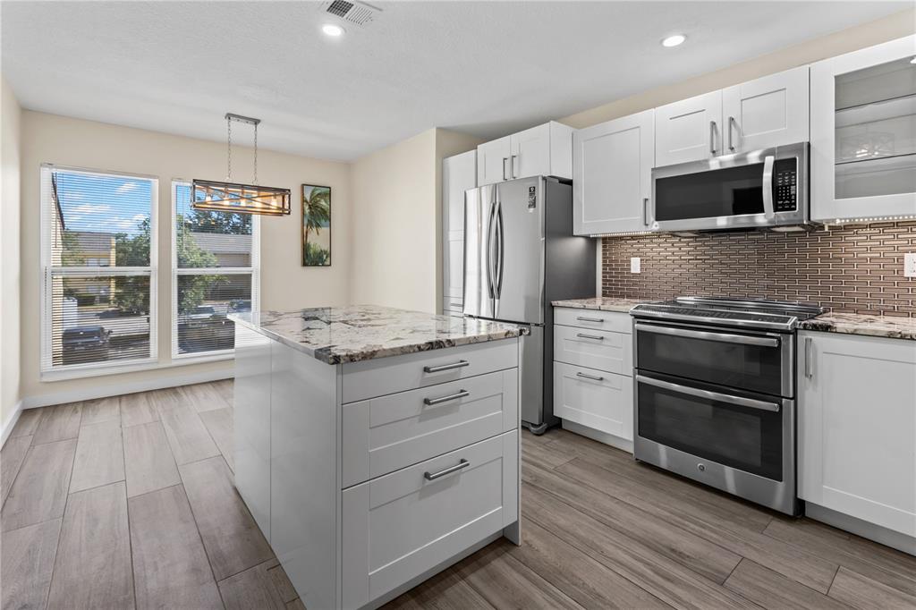 A kitchen features white cabinets, stainless steel appliances, a granite-topped island, and wood-look tile flooring — 3405 CLARK ROAD UNIT 205, SARASOTA, FL