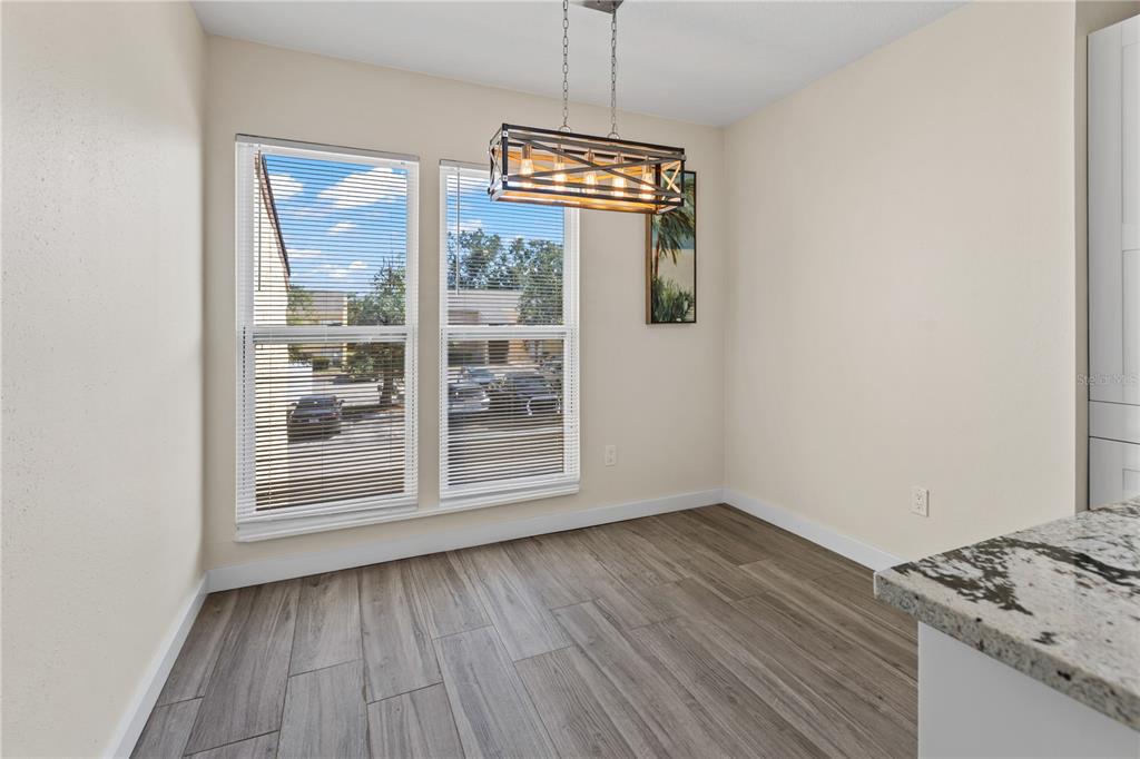 A dining area features wood-look tile flooring, two windows with blinds, and a rectangular light fixture — 3405 CLARK ROAD UNIT 205, SARASOTA, FL