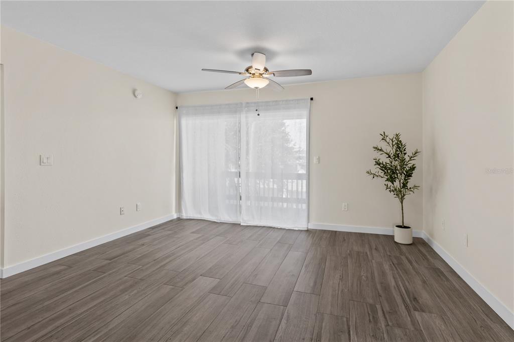 An empty living room features wood-look tile flooring, a ceiling fan, and sliding glass doors — 3405 CLARK ROAD UNIT 205, SARASOTA, FL