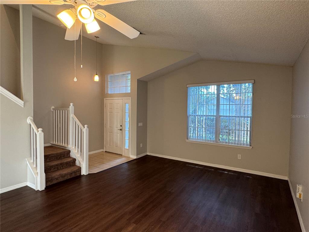 A living room features dark wood-look flooring, a vaulted ceiling, a staircase, and a front door — 4944 WATERSIDE PIONTE CIRCLE, ORLANDO, FL