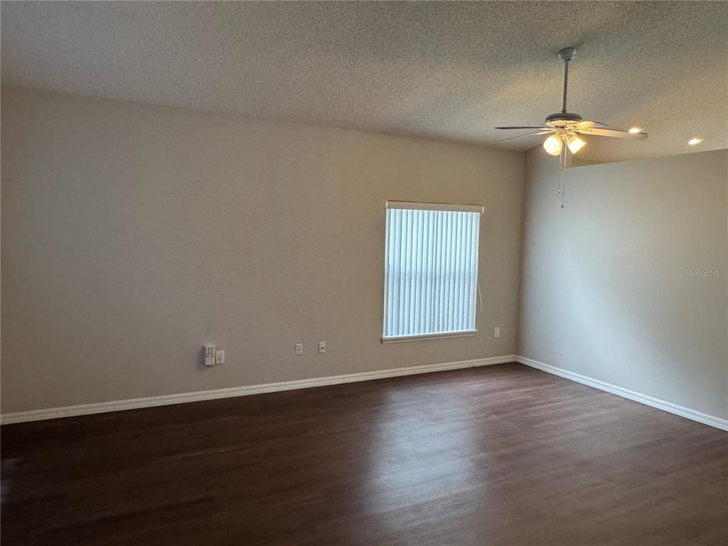 An empty room features dark wood-look flooring, light-colored walls, a ceiling fan, and a window — 4944 WATERSIDE PIONTE CIRCLE, ORLANDO, FL