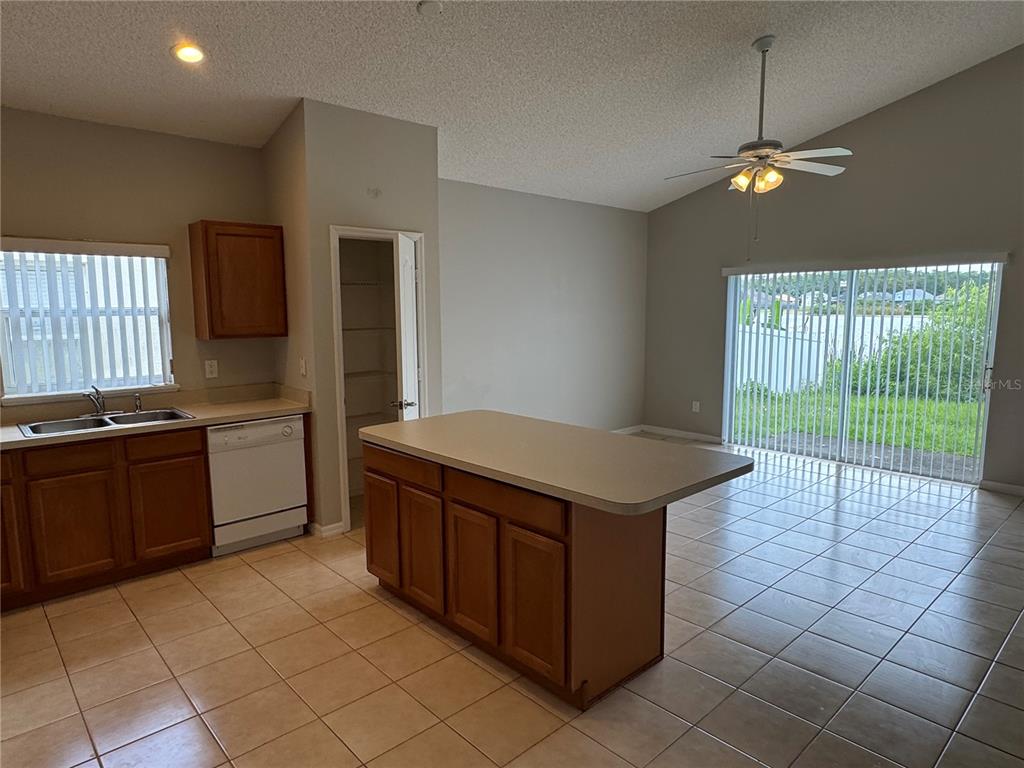 A kitchen with wooden cabinets, a central island, and tile flooring opens to a dining area — 4944 WATERSIDE PIONTE CIRCLE, ORLANDO, FL
