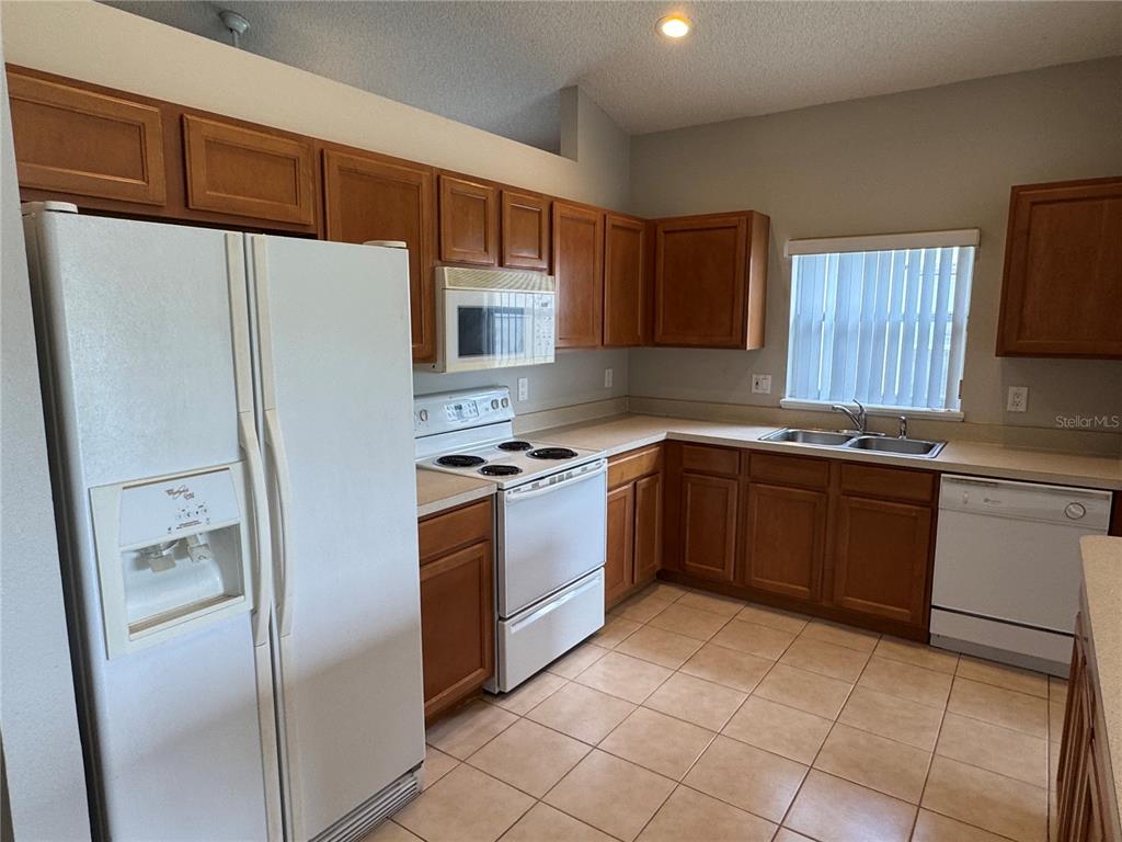 A kitchen with wood cabinets, white appliances, tile flooring, and a double sink — 4944 WATERSIDE PIONTE CIRCLE, ORLANDO, FL