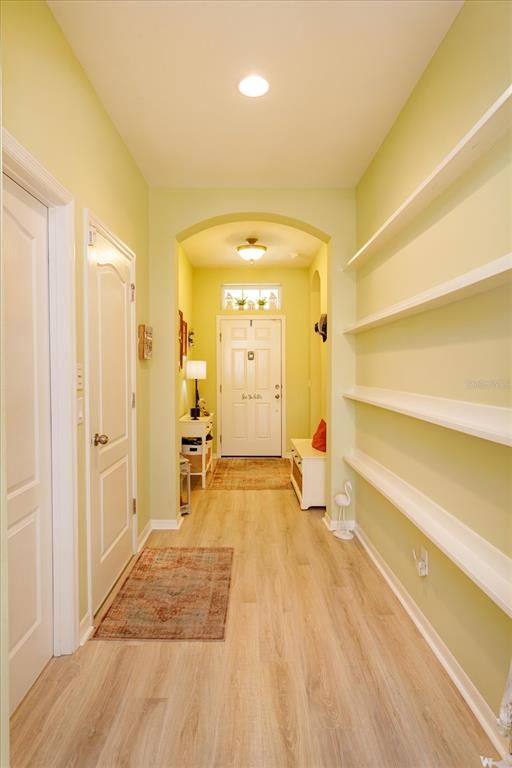 A hallway with light wood flooring, pale green walls, built-in shelving, and a white front door — 12789 BOSWORTH AVENUE, WINDERMERE, FL