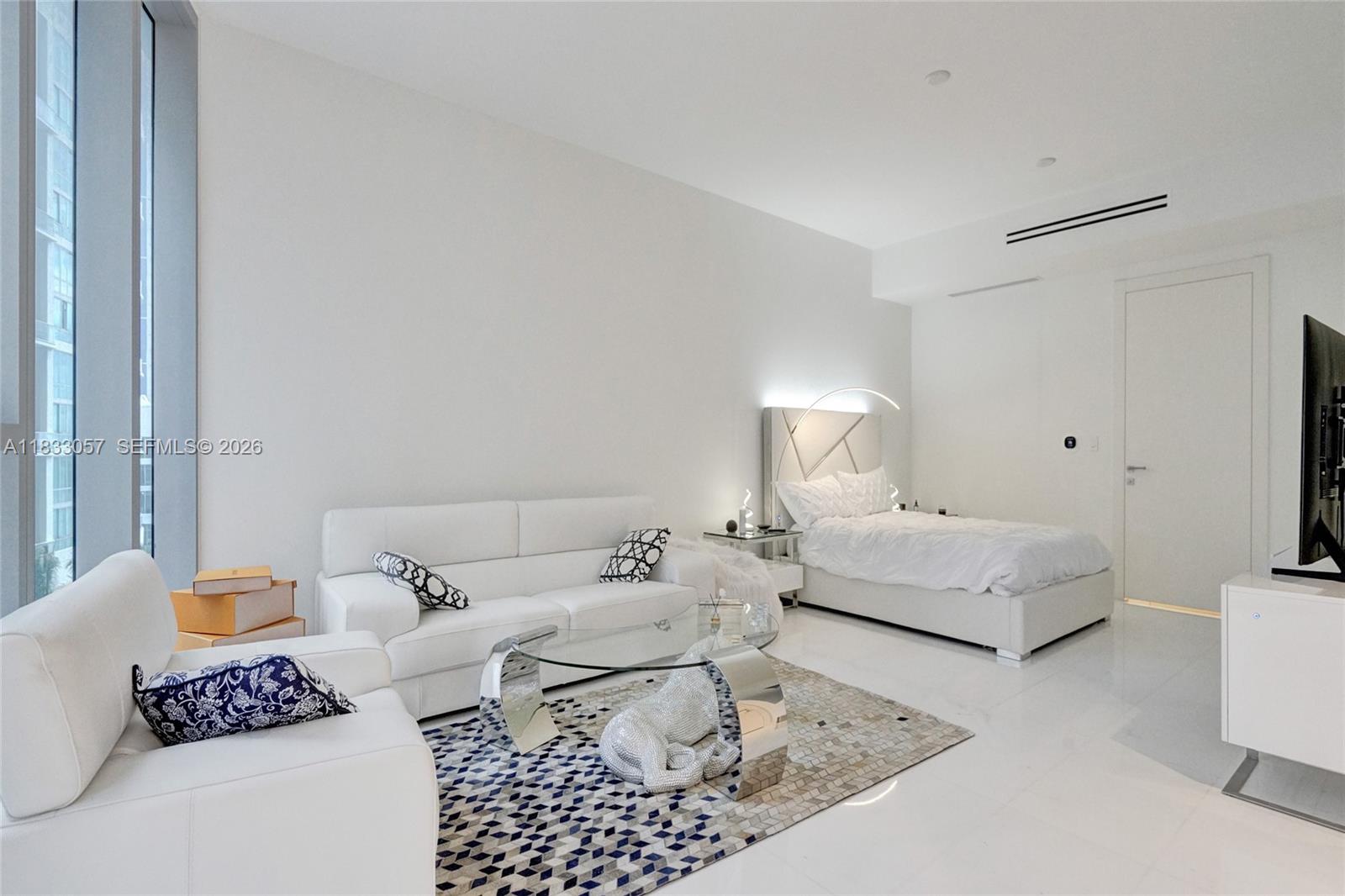 A modern studio apartment features white furniture, a bed, a sofa, and floor-to-ceiling windows — 300 Biscayne Blvd Way # 505C, Miami FL 33131, MIAMI, FL