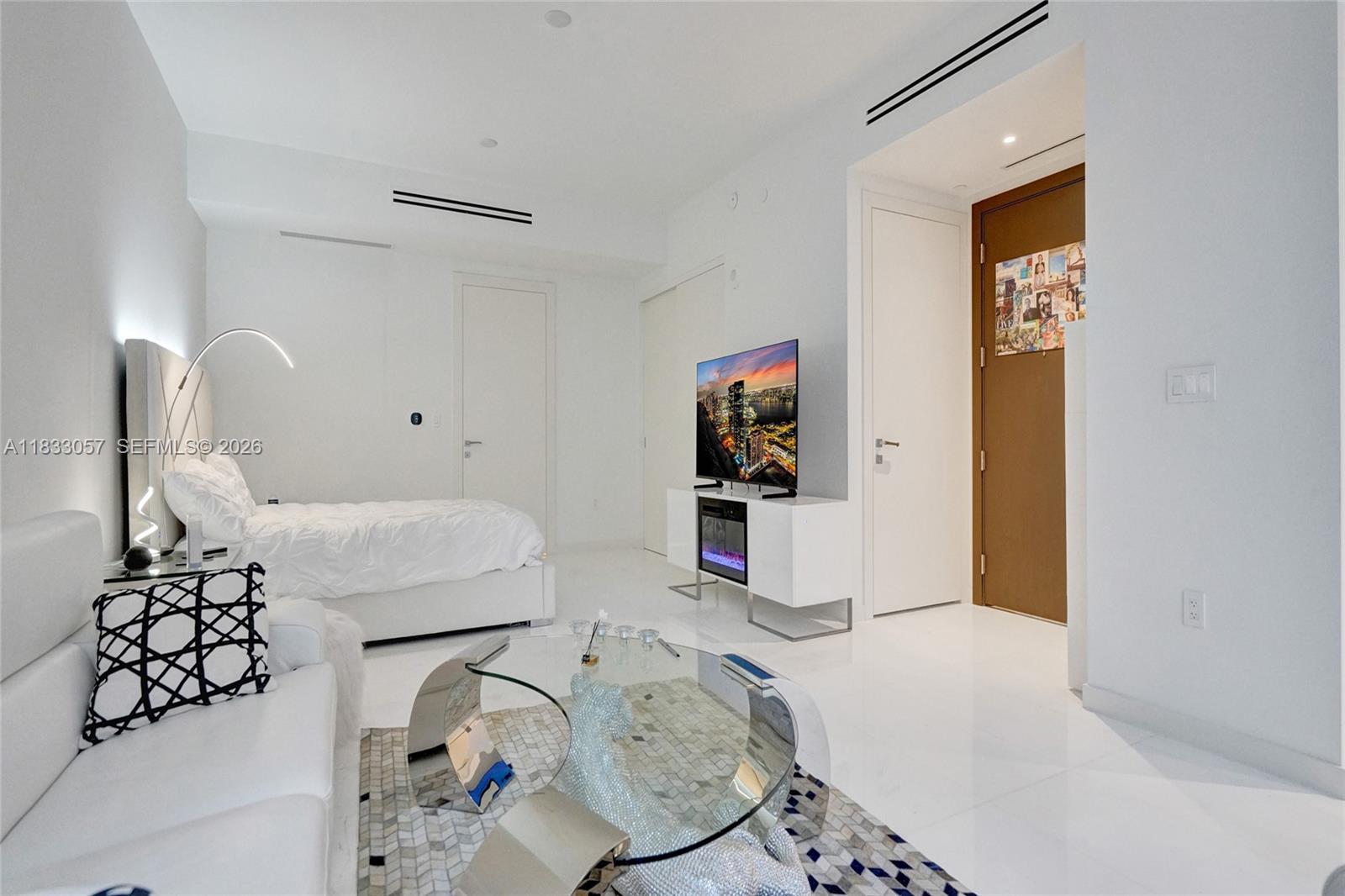 A modern studio apartment features white tile floors, a bed, a sofa, and a television — 300 Biscayne Blvd Way # 505C, Miami FL 33131, MIAMI, FL