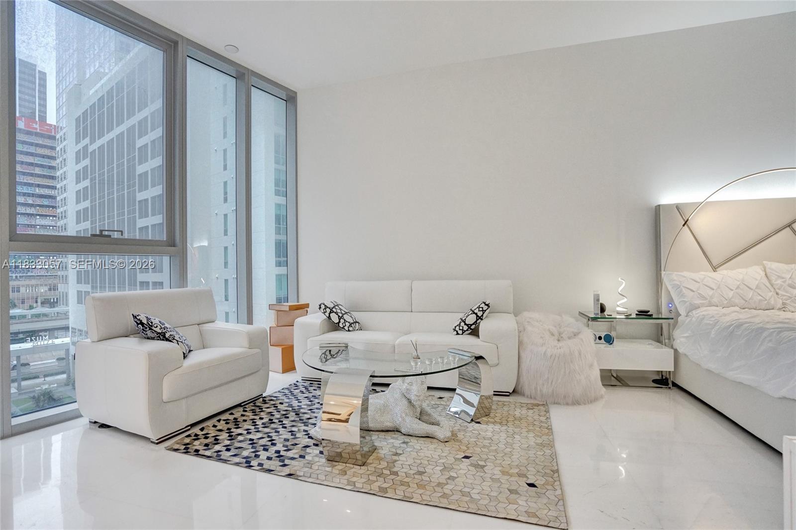 A modern studio apartment features white furniture, a patterned rug, and floor-to-ceiling windows — 300 Biscayne Blvd Way # 505C, Miami FL 33131, MIAMI, FL