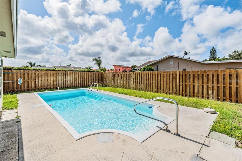 A rectangular swimming pool with a metal handrail sits in a fenced backyard — 11440 130TH AVENUE, LARGO, FL