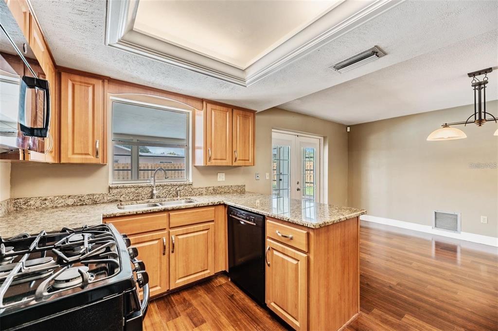A kitchen with wood cabinets, granite countertops, a black dishwasher, and hardwood flooring — 11440 130TH AVENUE, LARGO, FL