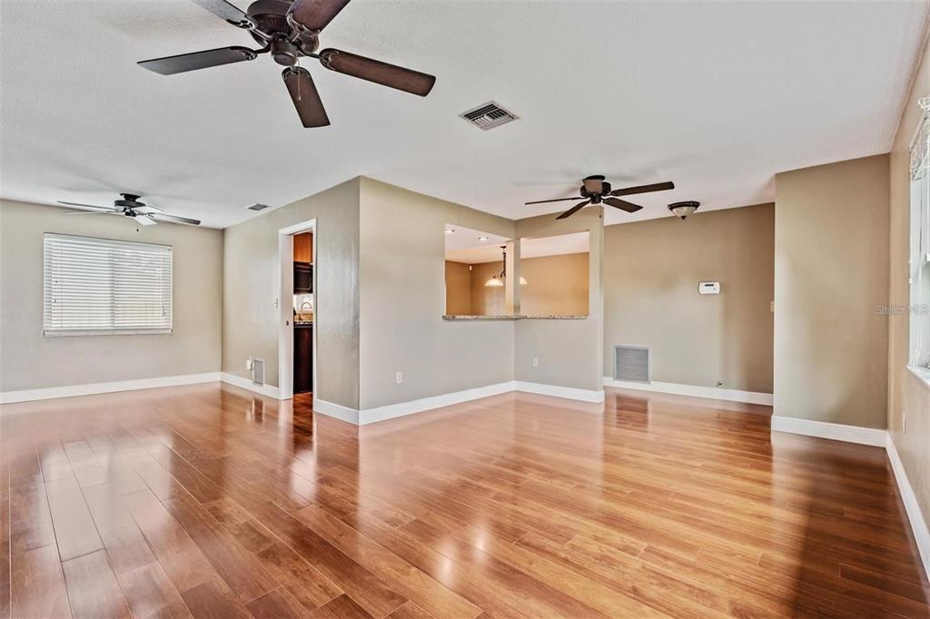An empty living room with hardwood floors, two ceiling fans, and a kitchen pass-through window — 11440 130TH AVENUE, LARGO, FL
