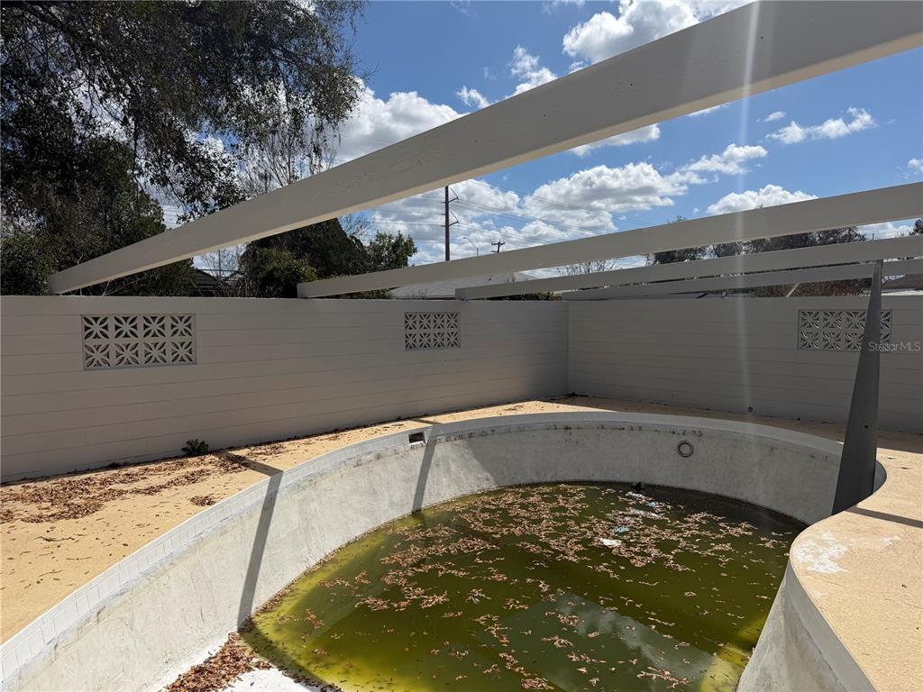 An empty, green-water swimming pool is enclosed by a privacy wall with decorative breeze blocks — 2105 SW 38TH COURT, OCALA, FL