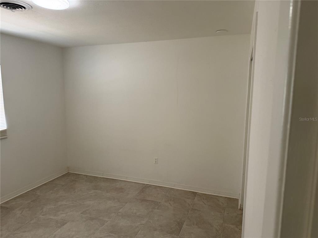 An empty room features white walls, a window with blinds, and light-colored tile flooring — 2105 SW 38TH COURT, OCALA, FL