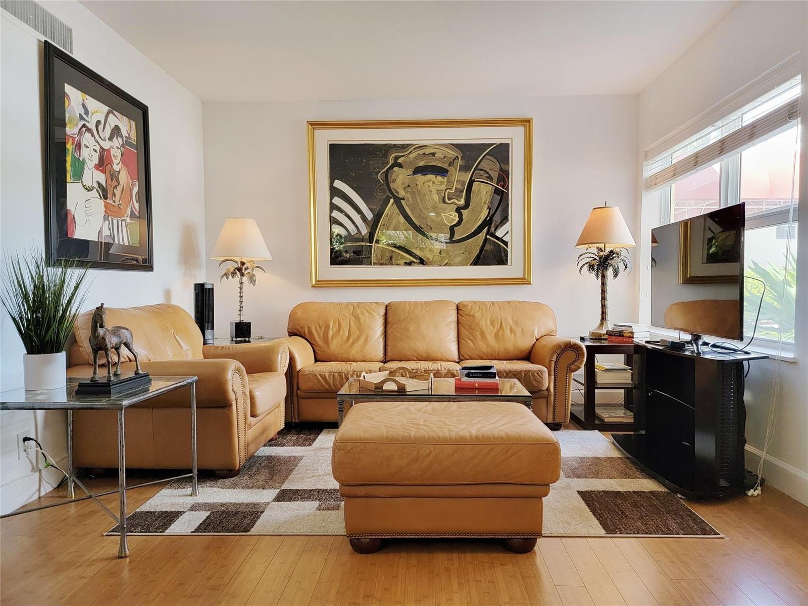 A living room features tan leather furniture, a patterned area rug, and two framed paintings — FORT LAUDERDALE, FL