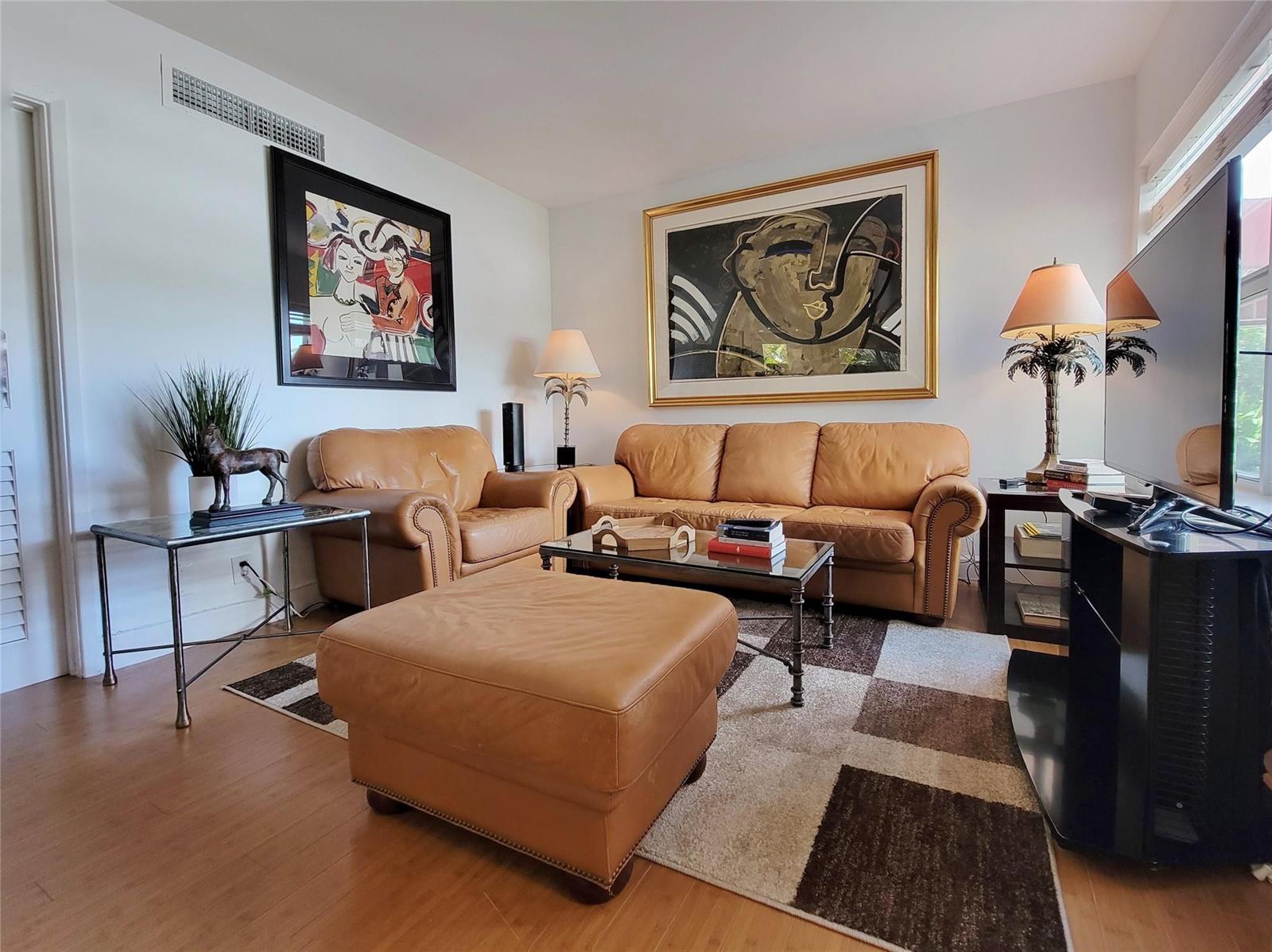 A living room features tan leather furniture, a glass coffee table, and two large framed paintings — FORT LAUDERDALE, FL