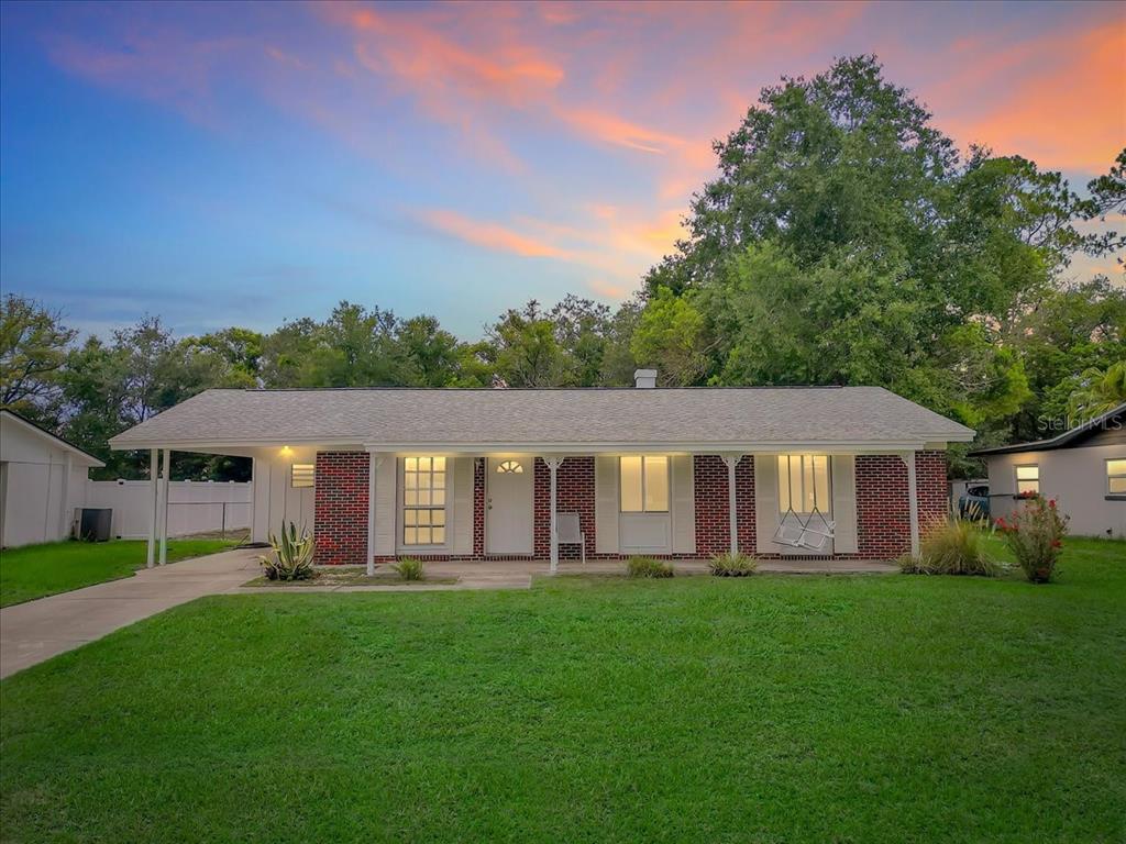 A single-story brick house with a front porch and attached carport under a sunset sky — 5810 DRIFTWOOD DRIVE, LAKELAND, FL