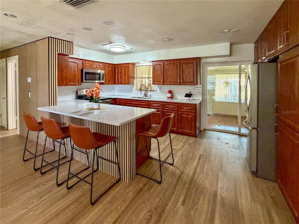 A kitchen with wood cabinets, a white island, and three bar stools on wood flooring — 45 CASWELL DRIVE, ORLANDO, FL
