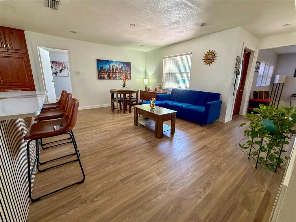 An open-concept living and dining area features wood-look flooring, a blue sofa, and bar seating — 45 CASWELL DRIVE, ORLANDO, FL