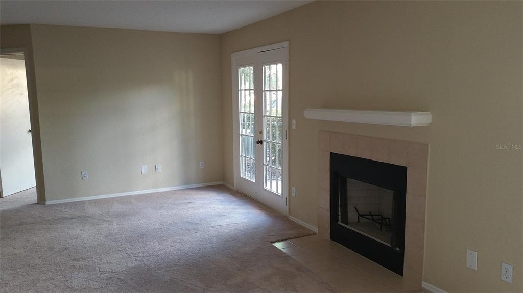 A living room features beige carpet, tan walls, a fireplace, and glass-paned double doors — 2550 N ALAFAYA TRAIL UNIT 7104, ORLANDO, FL