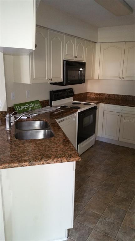 A kitchen with white cabinets, granite countertops, a double sink, and black appliances — 2550 N ALAFAYA TRAIL UNIT 7104, ORLANDO, FL